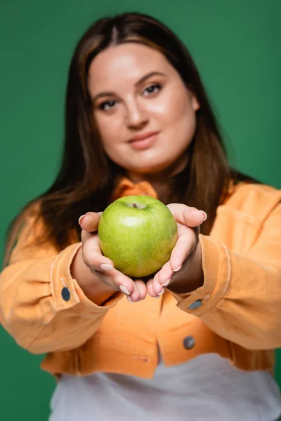 Apple in hands of woman with overweight on blurred background isolated on green — Stock Photo