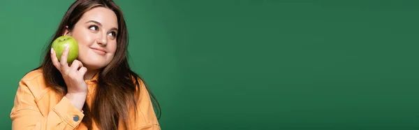 Красивая брюнетка женщина с избыточным весом держа свежее яблоко изолированы на зеленый, баннер — стоковое фото