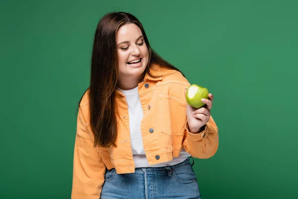 Cheerful body positive woman looking at apple isolated on green — Stock Photo