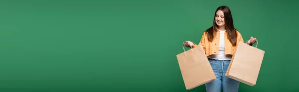 Mujer feliz con sobrepeso sosteniendo bolsas aisladas en verde, pancarta - foto de stock