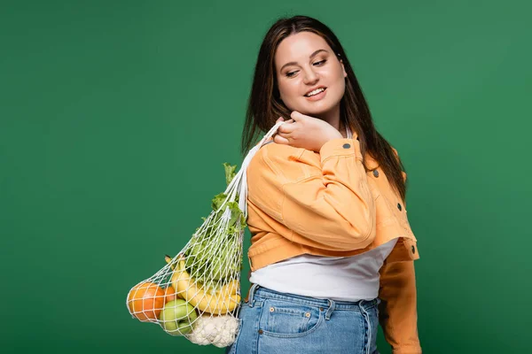 Femme heureuse avec sac de filet de maintien en surpoids avec des aliments frais isolés sur vert — Photo de stock