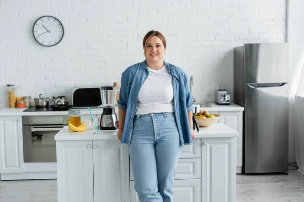 Donna sorridente con sovrappeso in piedi vicino al cibo in cucina — Foto stock