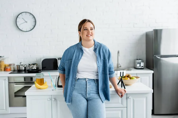 Happy woman with overweight standing near kitchen table with cellphone and food — Stock Photo