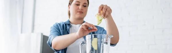 Blurred woman with overweight putting apple slices in blender in kitchen, banner — Stock Photo