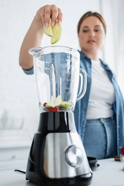 Mulher desfocada com sobrepeso colocando frutas no liquidificador — Fotografia de Stock