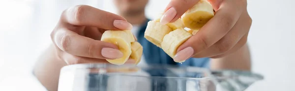 Vue recadrée d'une femme floue tenant des tranches de banane près du mélangeur, bannière — Photo de stock