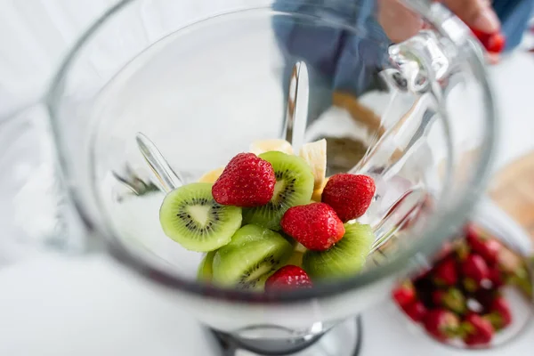 Cropped view of fresh fruits in blender near blurred woman in kitchen — Stock Photo