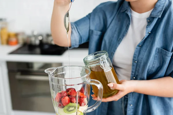 Vista recortada de mujer de talla grande vertiendo miel en licuadora con frutas - foto de stock