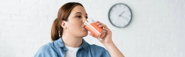 Plus size woman drinking fruit smoothie in kitchen, banner — Stock Photo