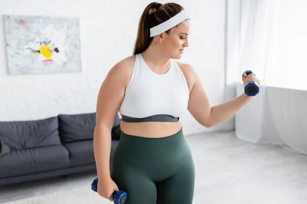 Side view of plus size woman training with dumbbell in living room — стоковое фото