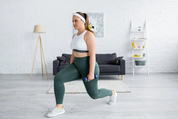 Brunette woman with overweight doing lunges with dumbbell at home — Stock Photo