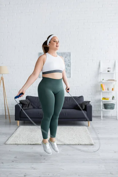 Jeune femme plus la taille sautant avec corde à sauter dans le salon — Photo de stock