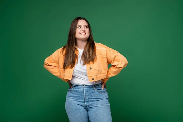 Fröhliche Plus-Size-Frau hält Hände auf Hüften isoliert auf Grün — Stockfoto