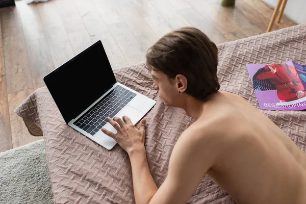 Vue grand angle de jeune homme transgenre torse nu utilisant un ordinateur portable avec écran blanc sur le lit — Photo de stock