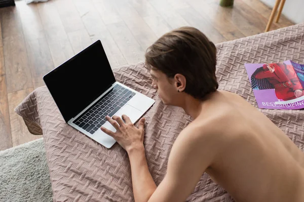 High angle view of shirtless transgender young man using laptop with blank screen on bed — Stock Photo