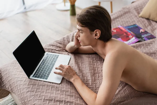 Vista de ángulo alto de hombre transgénero sin camisa utilizando el ordenador portátil con pantalla en blanco en la cama - foto de stock