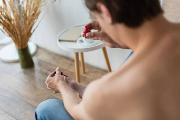 Desenfocado y sin camisa joven transgénero haciendo pedicura en el dormitorio - foto de stock