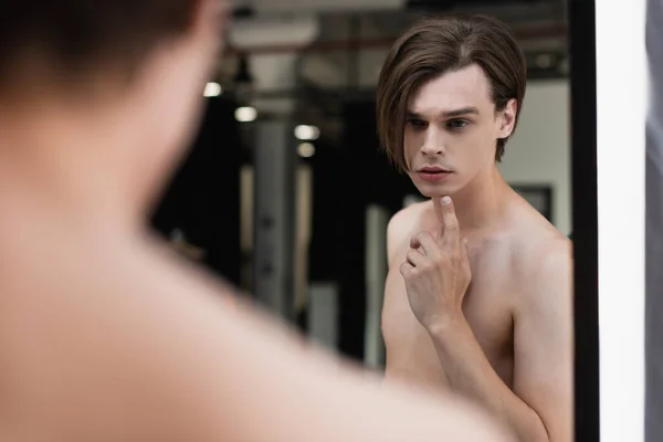 Sin camisa transgénero joven mirando el espejo - foto de stock