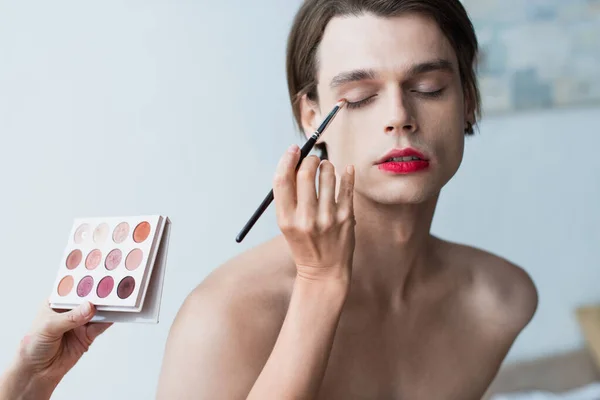 Makeup artist applying eye shadow on transgender man — Stock Photo