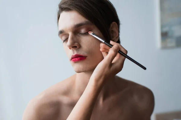 Maquiador aplicando sombra nos olhos em homem transexual com escova cosmética — Fotografia de Stock