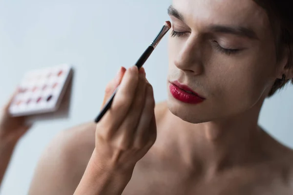 Trucco artista applicando ombretto sull'uomo transgender con pennello cosmetico — Foto stock