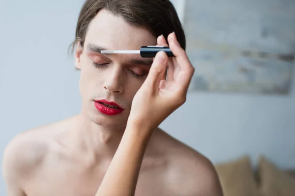 Maquillador aplicando gel de cejas en hombre transgénero - foto de stock