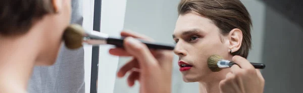 Hombre transgénero joven aplicando polvo facial cerca del espejo, pancarta - foto de stock