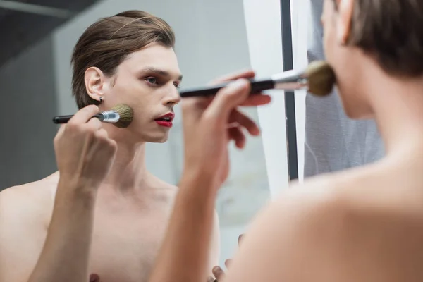 Jeune homme transgenre appliquant de la poudre visage près du miroir — Photo de stock