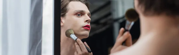 Hombre transgénero joven aplicando polvo facial en el cuello cerca del espejo, pancarta - foto de stock