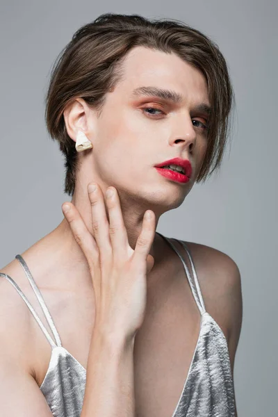 Молодой трансгендер с макияжем и серьгой позирует изолированно на сером — стоковое фото
