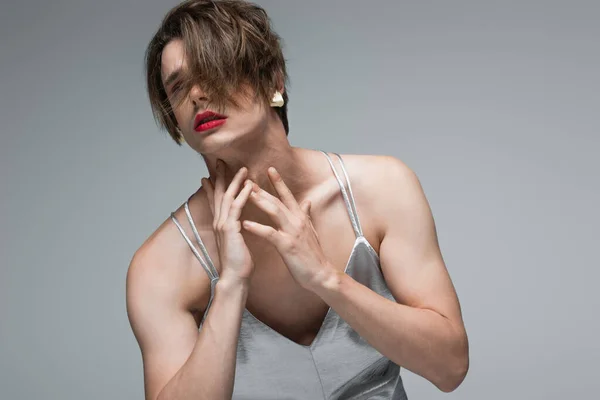 Hombre transgénero con maquillaje y pendiente posando en vestido de deslizamiento aislado en gris - foto de stock