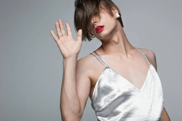 Молодий транссексуал з червоними губами і сережками позує в сукні ковзання ізольовано на сірому — стокове фото