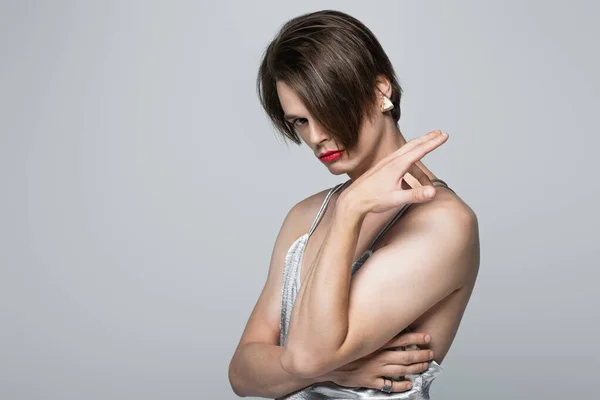 Homme transgenre avec lèvres rouges et boucle d'oreille posant en robe glissante isolé sur gris — Photo de stock