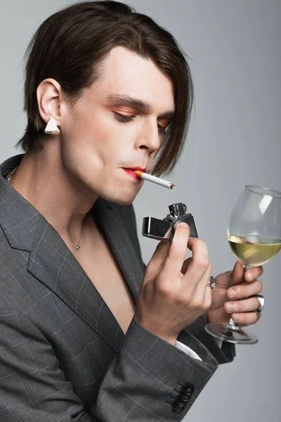 Jovem transexual homem segurando copo de vinho e isqueiro enquanto fuma isolado em cinza — Fotografia de Stock