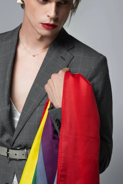 Junger transsexueller Mann im Blazer hält LGBT-Fahne isoliert auf grau — Stockfoto