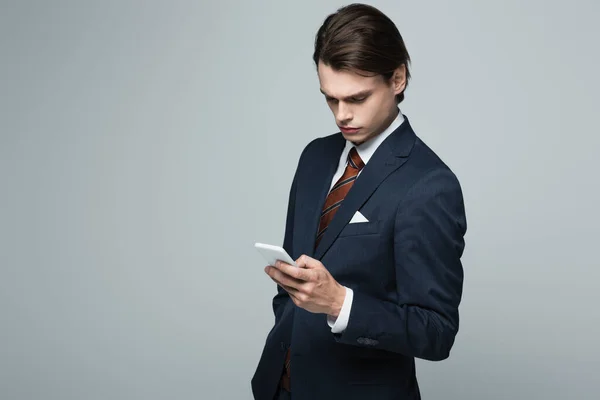 Молодий бізнесмен у костюмі, використовуючи смартфон ізольований на сірому — стокове фото
