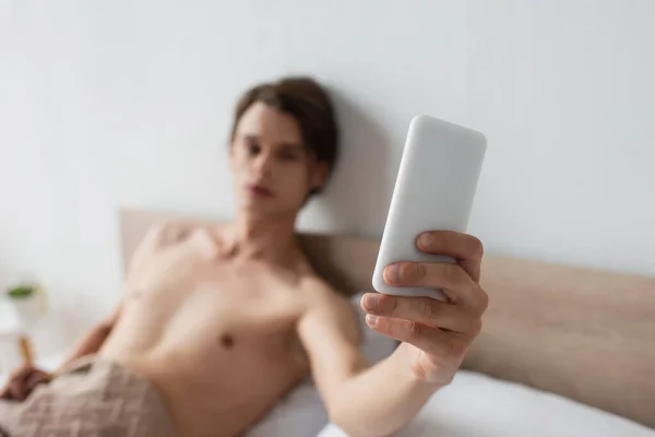 Размытый и без рубашки трансгендерный мужчина делает селфи на смартфоне — стоковое фото