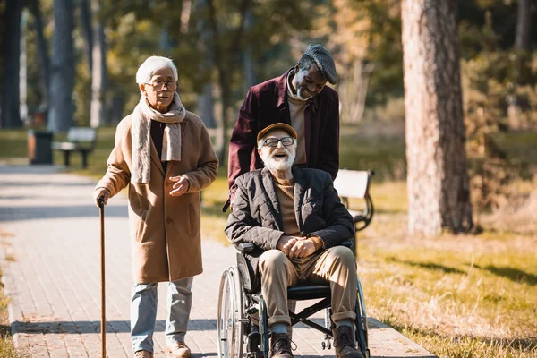 Веселый человек в инвалидной коляске рядом с межрасовыми друзьями в осеннем парке — стоковое фото