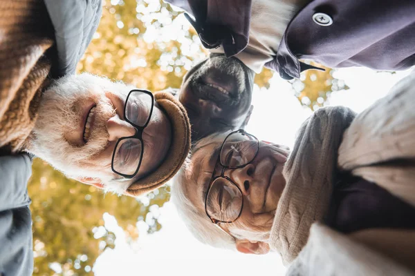 Bottom view of multicultural friends in eyeglasses looking at camera outdoors — Stock Photo