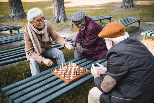 Веселі міжрасові чоловіки дивляться на друга біля шахів у парку — стокове фото