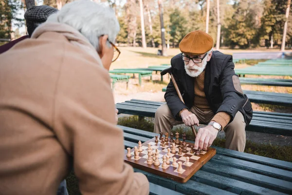 Пожилые мужчины играют в шахматы на скамейке запасных в осеннем парке — стоковое фото