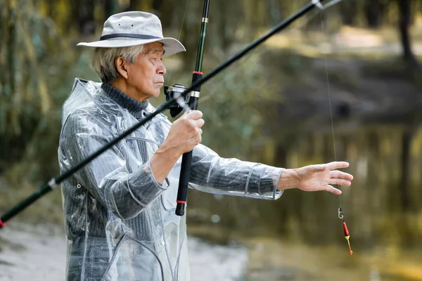 Asiatico uomo holding fishing rod near blurred lago — Foto stock