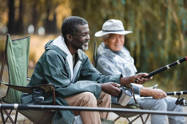 Позитивный африканский американец держит термостат и удочку рядом с размытым другом — стоковое фото