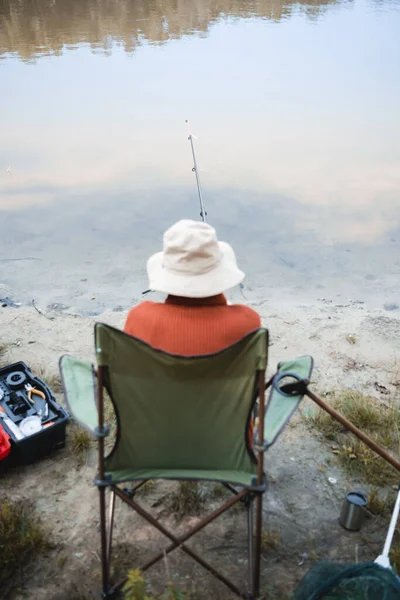 Rückansicht eines verschwommenen Seniors beim Angeln in der Nähe von Spazierstock und See an der Küste — Stockfoto