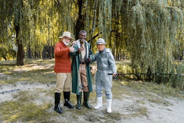 Lächelnde Männer mit Angelruten und Fischen wie vor der Kamera im Freien — Stockfoto