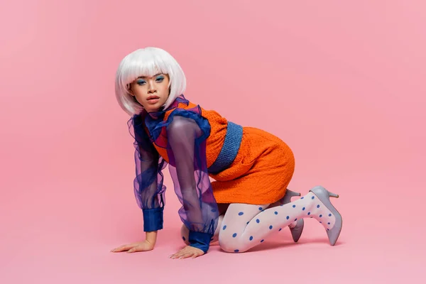 Жінка азіатського поп-мистецтва в підборах взуття, що стоїть на колінах на рожевому фоні — стокове фото