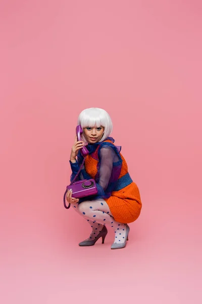 Lächelndes asiatisches Pop-Art-Model blickt in die Kamera, während es auf rosa Hintergrund telefoniert — Stockfoto