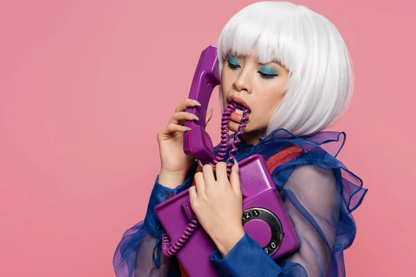 Stilvolle asiatische Pop-Art-Frau beißt Kabel und spricht auf Vintage-Telefon isoliert auf rosa — Stockfoto