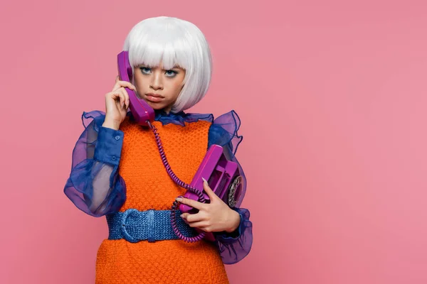 Molesto asiático pop arte mujer hablando en retro teléfono aislado en rosa - foto de stock