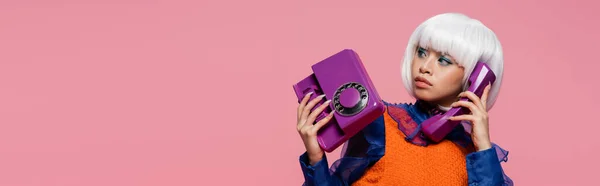 Азиатская модель поп-арта разговаривает по телефону и отводит глаза в сторону на розовом баннере — стоковое фото
